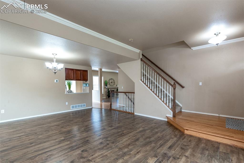 Unfurnished living room with dark wood finished floors, a chandelier, stairway, and crown molding