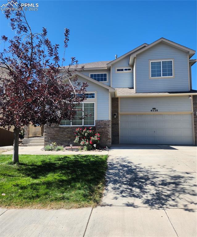 View of front of home featuring concrete driveway, a front lawn, an attached garage, stone siding, and a shingled roof