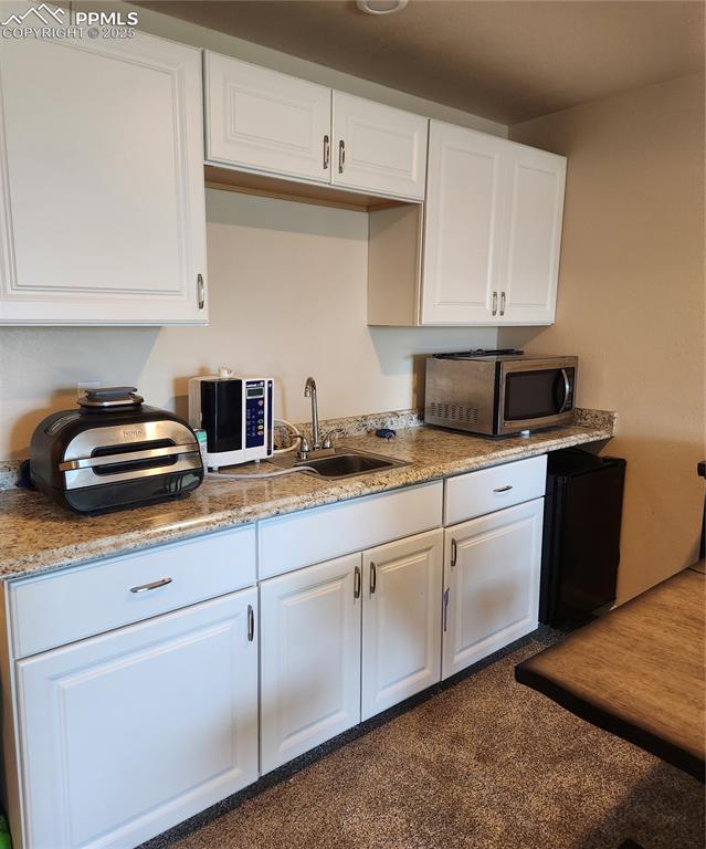 Wet bar , kitchen with refrigerator in the basement cabinets, light stone counters, refrigerator, and dark carpet