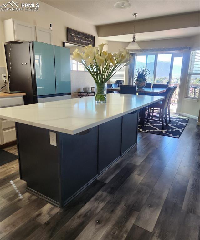 Kitchen featuring fridge, decorative light fixtures, dark wood finished floors, a kitchen island, and a kitchen bar