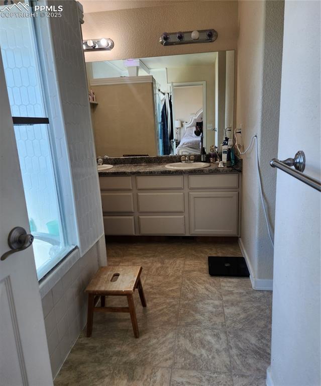 Full bath with ensuite bath, double vanity, bath tub, a textured wall, and tile patterned flooring