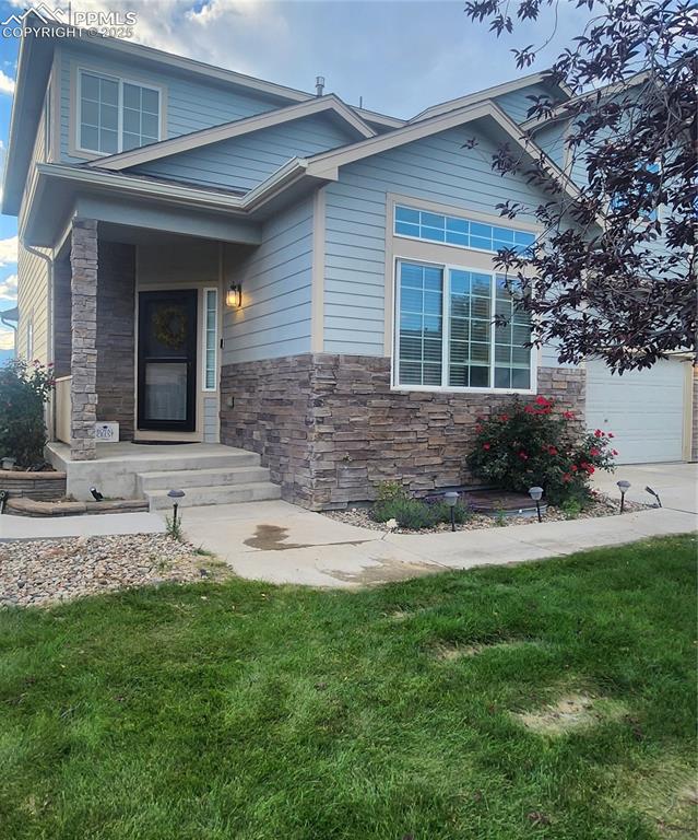 View of front facade with stone siding, a garage, and a front lawn