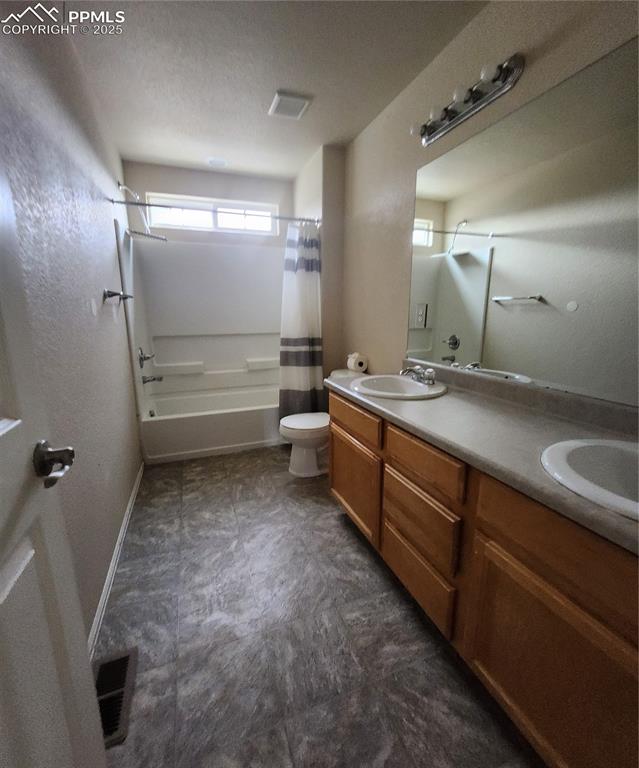 Bathroom featuring double vanity, shower / tub combo, a textured ceiling, and dark flooring