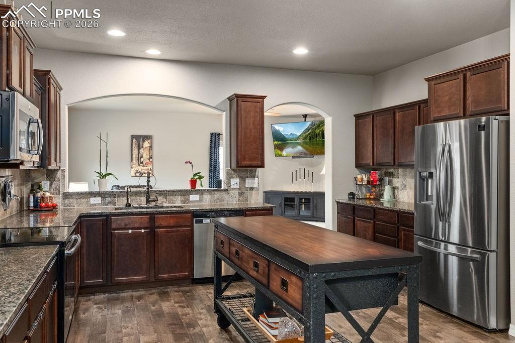 Kitchen with stainless steel appliances, dark wood finish cabinets, dark wood flooring, dark granite counters, and recessed lighting