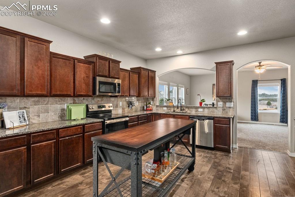 Kitchen with stainless steel appliances, dark wood finish cabinets, dark wood flooring, dark granite counters, and recessed lighting