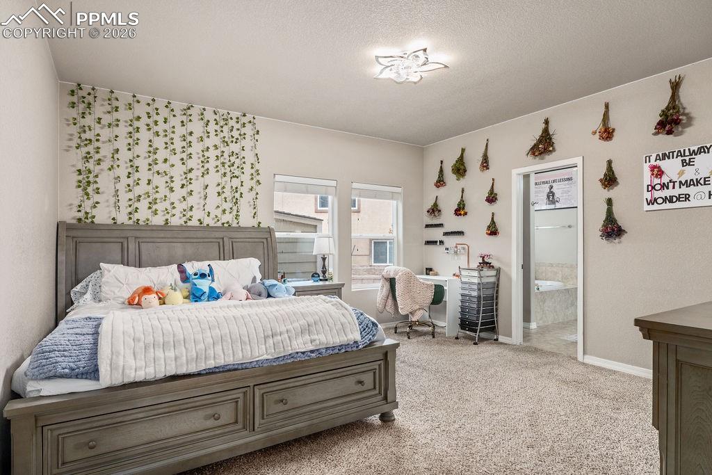 Main floor primary bedroom featuring light colored carpet, a textured ceiling, and ensuite bathroom