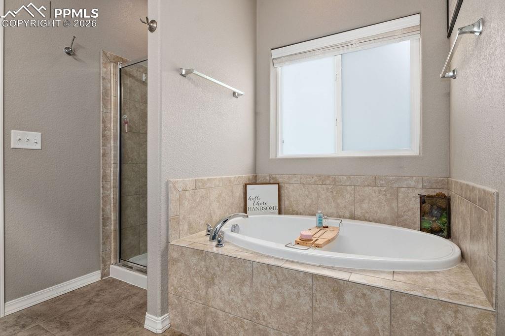 Main floor primary bathroom featuring a stall shower, a bath, a textured wall, and tile patterned floors