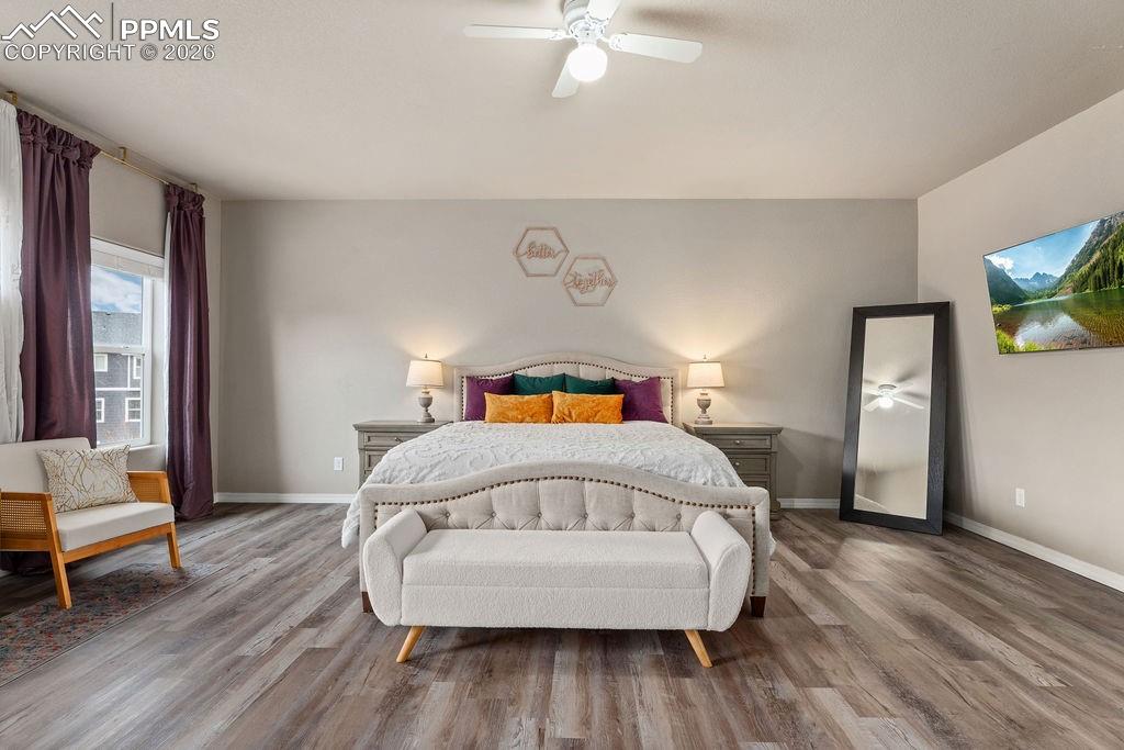 Upper floor primary bedroom with wood finished floors and a ceiling fan