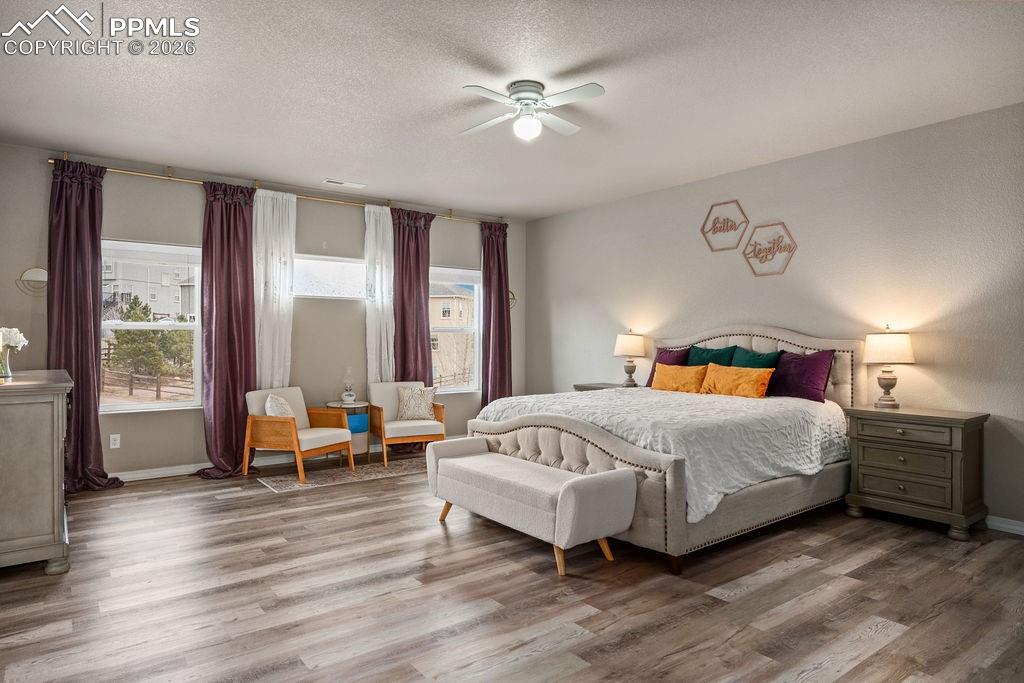 Upper floor primary bedroom with a textured ceiling, wood finished floors, and ceiling fan
