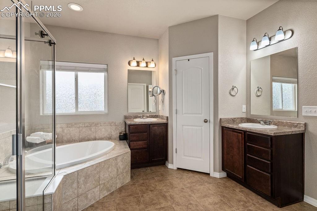 Full bathroom with two vanities, a bath, a shower stall, and light tile patterned floors