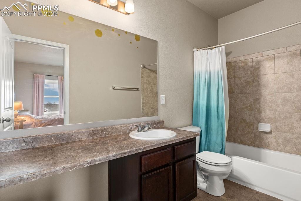 Ensuite bathroom with vanity, shower / tub combo with curtain, tile patterned flooring, and a textured wall
