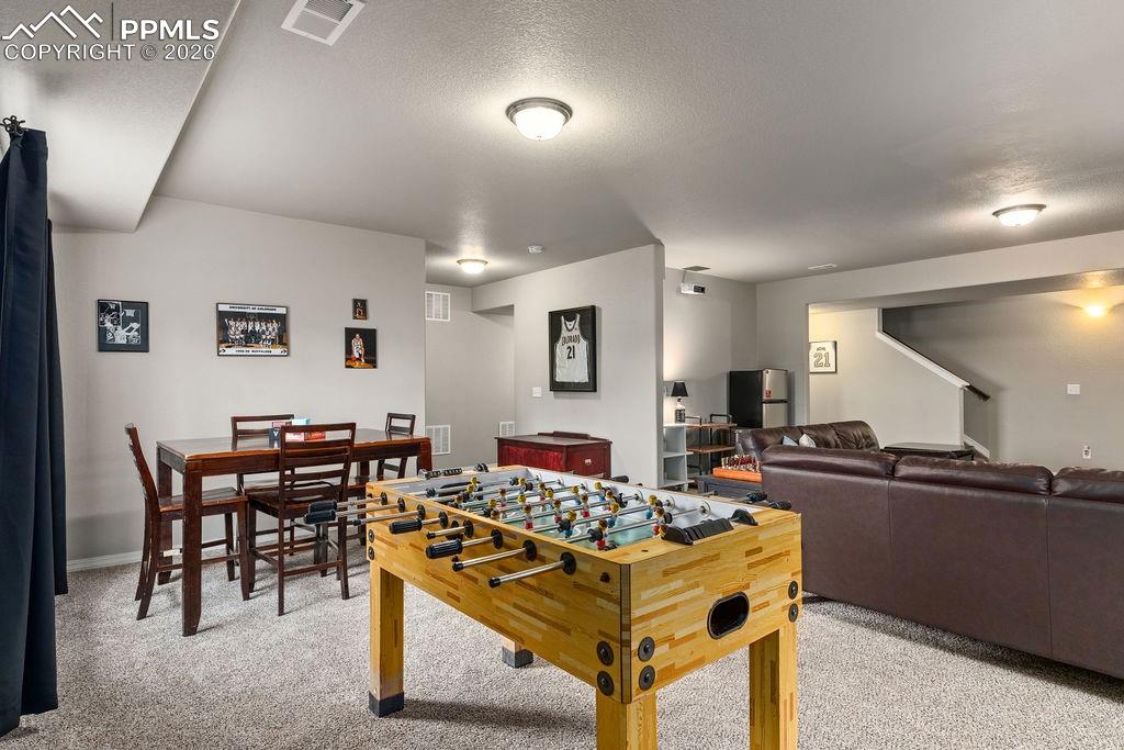 Basement recreation room featuring light carpet and a textured ceiling
