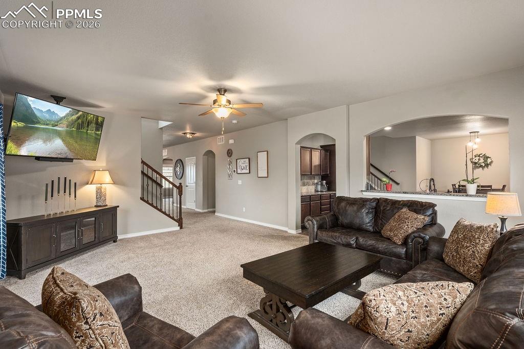 Carpeted living room featuring arched walkways and a ceiling fan