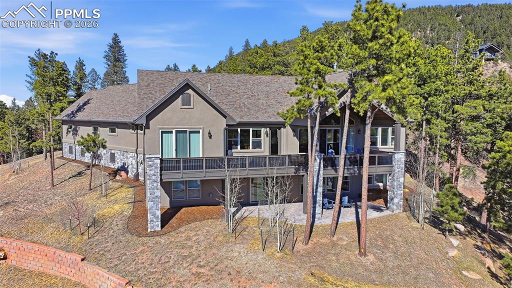 Rear view of property with stucco siding, a patio area, stone siding, and roof with shingles