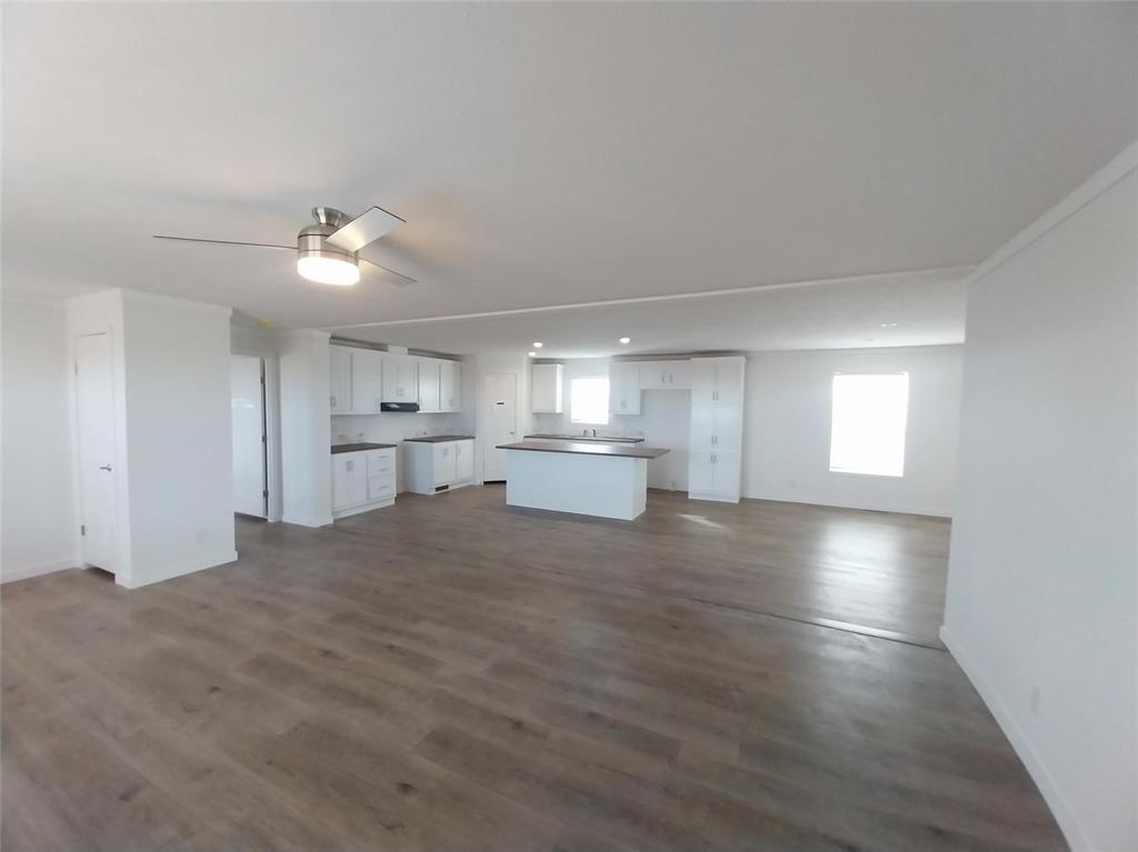 Unfurnished living room with plenty of natural light, dark wood-type flooring, a ceiling fan, and crown molding