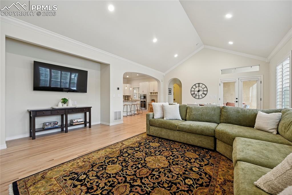 Living area with arched walkways, light wood-style floors, ornamental molding, french doors, and recessed lighting