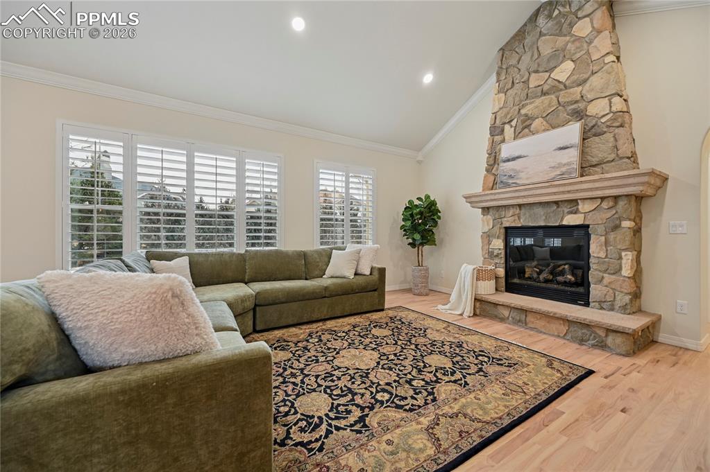Living room featuring vaulted ceiling, a fireplace, light wood-style flooring, crown molding, and recessed lighting