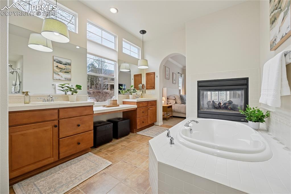 Bathroom featuring a bath, vanity, light tile patterned flooring, a high ceiling, and a multi sided fireplace