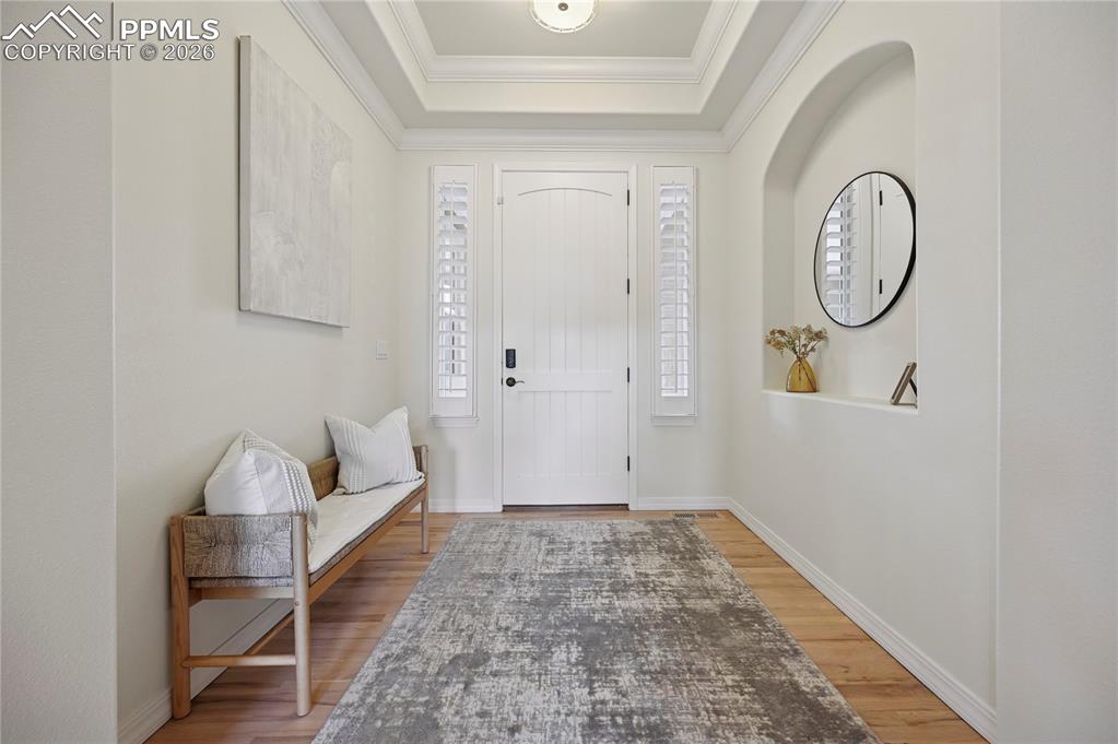 Foyer entrance featuring a raised ceiling, light wood-style flooring, and crown molding