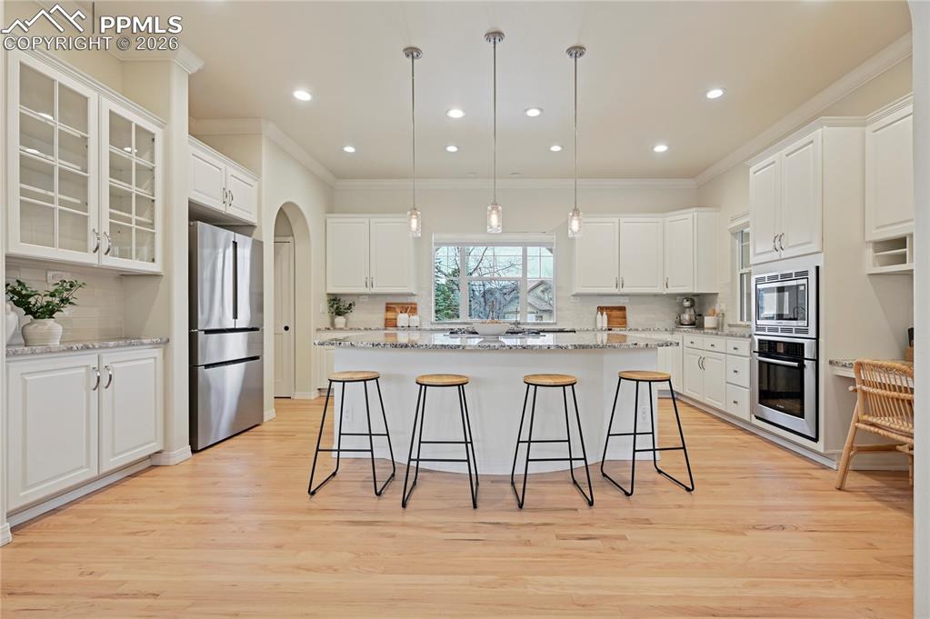 Kitchen featuring decorative light fixtures, a breakfast bar, white cabinetry, stainless steel appliances, and ornamental molding