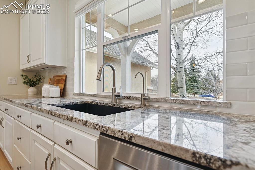 Kitchen featuring light stone counters, white cabinetry, and dishwasher