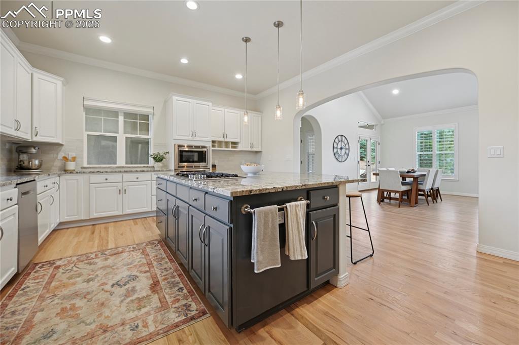 Dual tone kitchen with dual tone cabinets, decorative backsplash, light stone counters, hanging light fixtures, and light wood-style floors