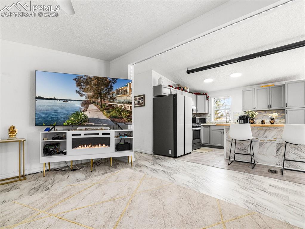 Kitchen featuring gray cabinets, a kitchen bar, a textured ceiling, light countertops, and freestanding refrigerator