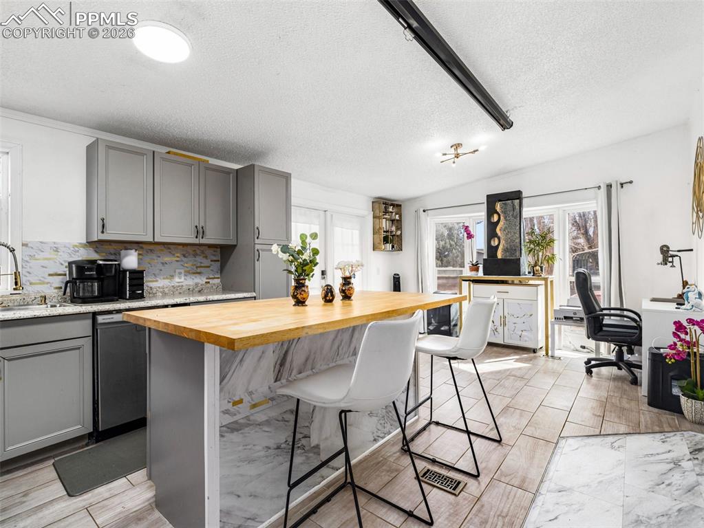 Kitchen with gray cabinetry, wooden counters, a breakfast bar area, tasteful backsplash, and a textured ceiling