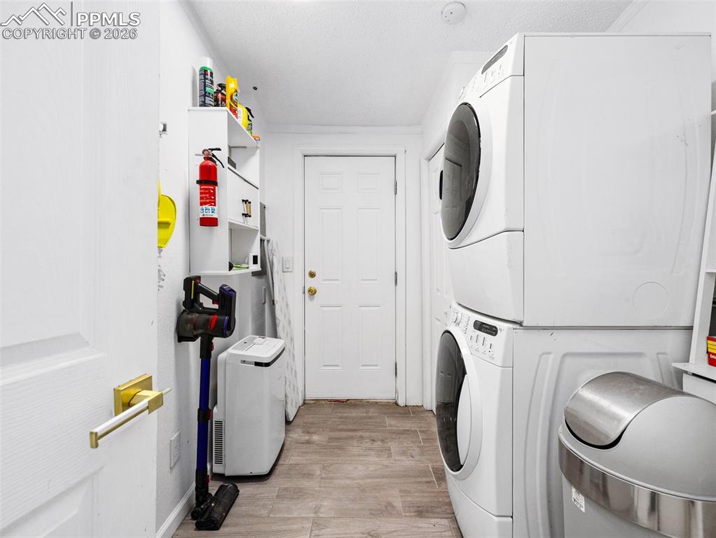 Laundry area with light wood-style flooring, stacked washer and dryer, and a textured ceiling