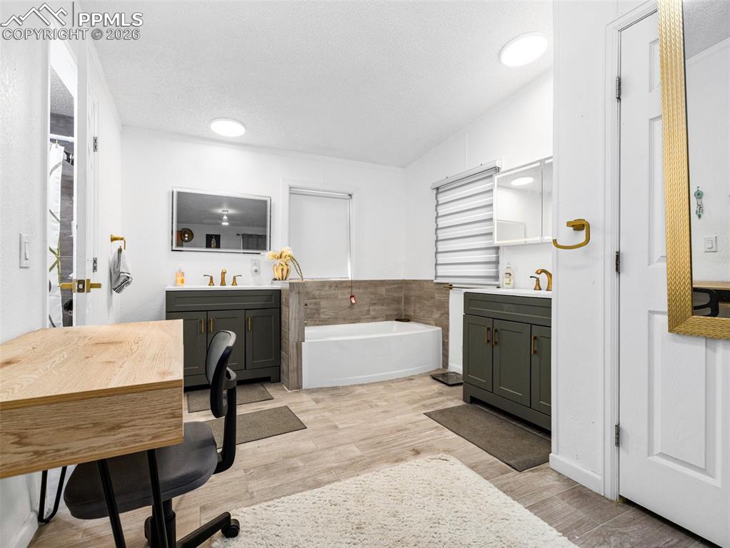 Full bathroom with two vanities, a textured ceiling, light wood-style floors, and a garden tub