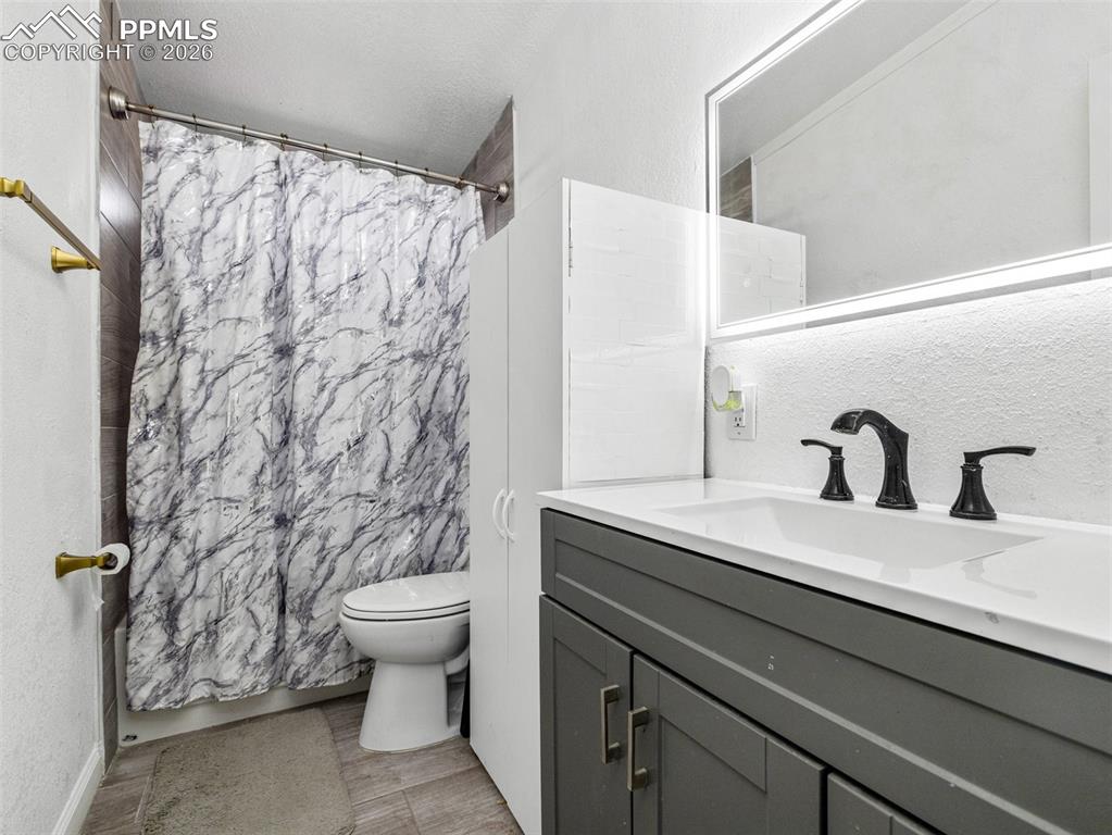 Full bath with a textured wall, vanity, a textured ceiling, shower / tub combo with curtain, and wood tiled floors