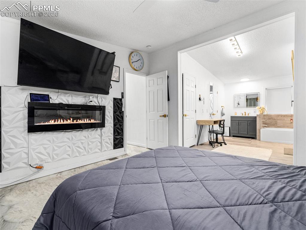 Bedroom featuring a textured ceiling, a glass covered fireplace, a ceiling fan, and connected bathroom