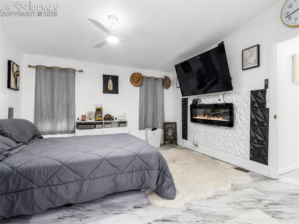 Bedroom with a textured ceiling, marble finish flooring, a ceiling fan, and a glass covered fireplace