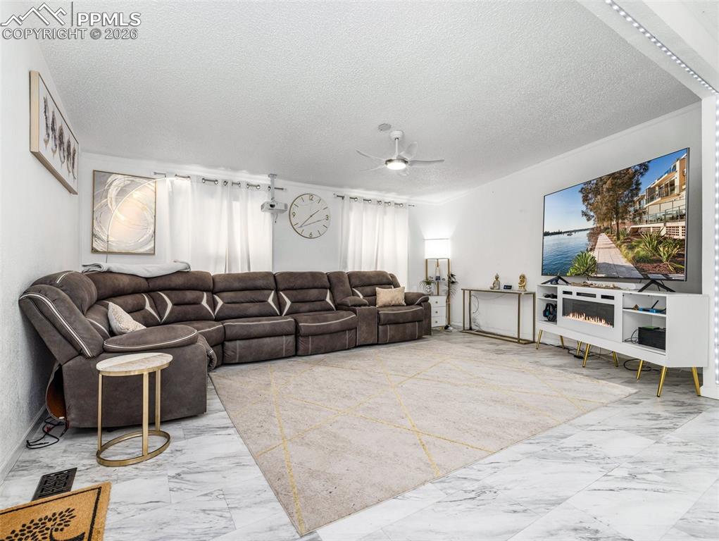 Living area featuring light marble finish floors, a textured ceiling, and a ceiling fan