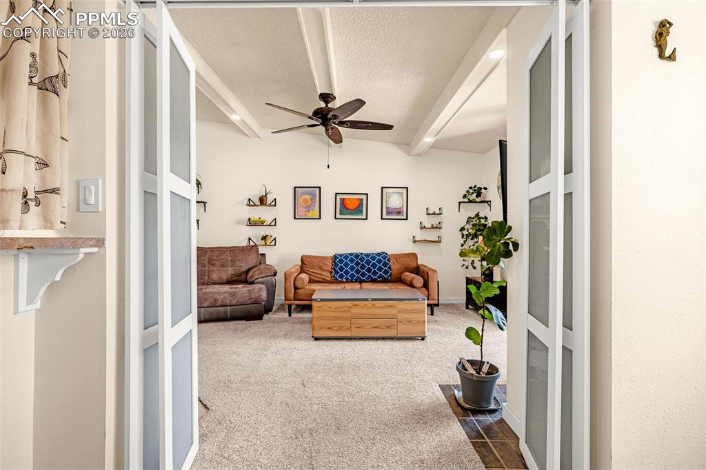 Carpeted living area featuring a ceiling fan, a textured ceiling, and beamed ceiling