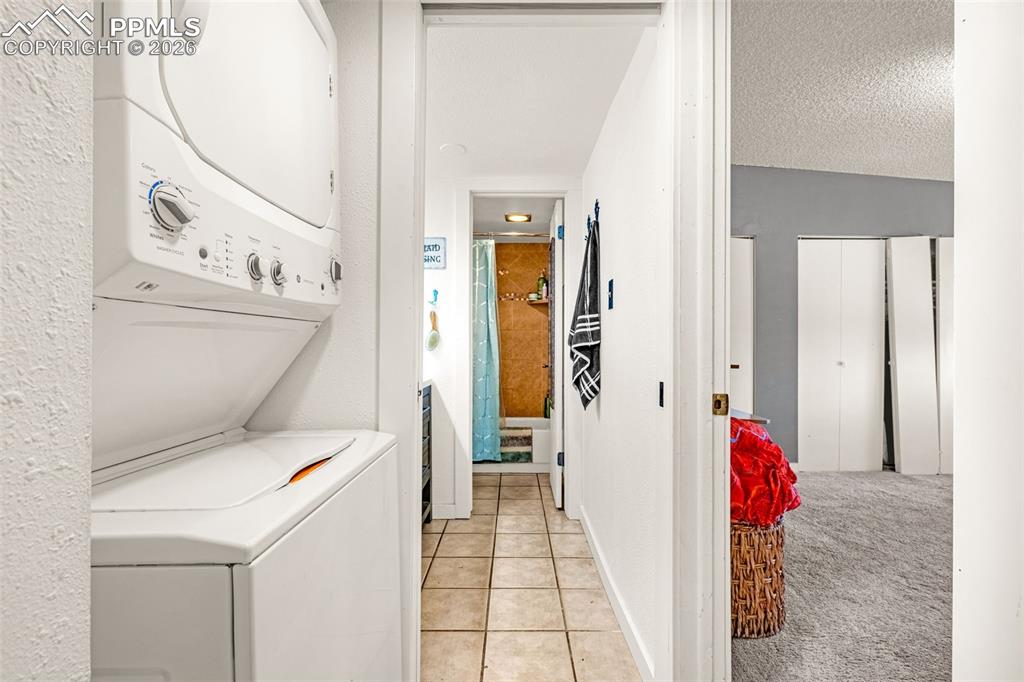 Laundry area featuring light carpet, stacked washer / drying machine, light tile patterned floors, and a textured ceiling
