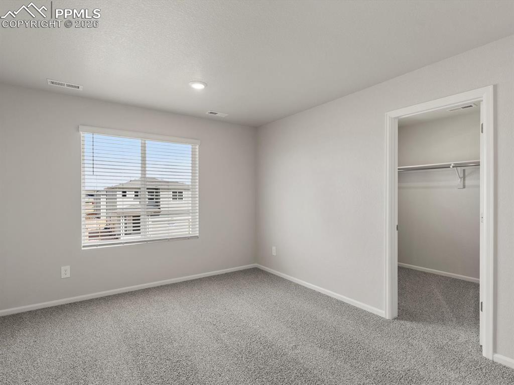 Unfurnished bedroom with a walk in closet, light colored carpet, and a textured ceiling