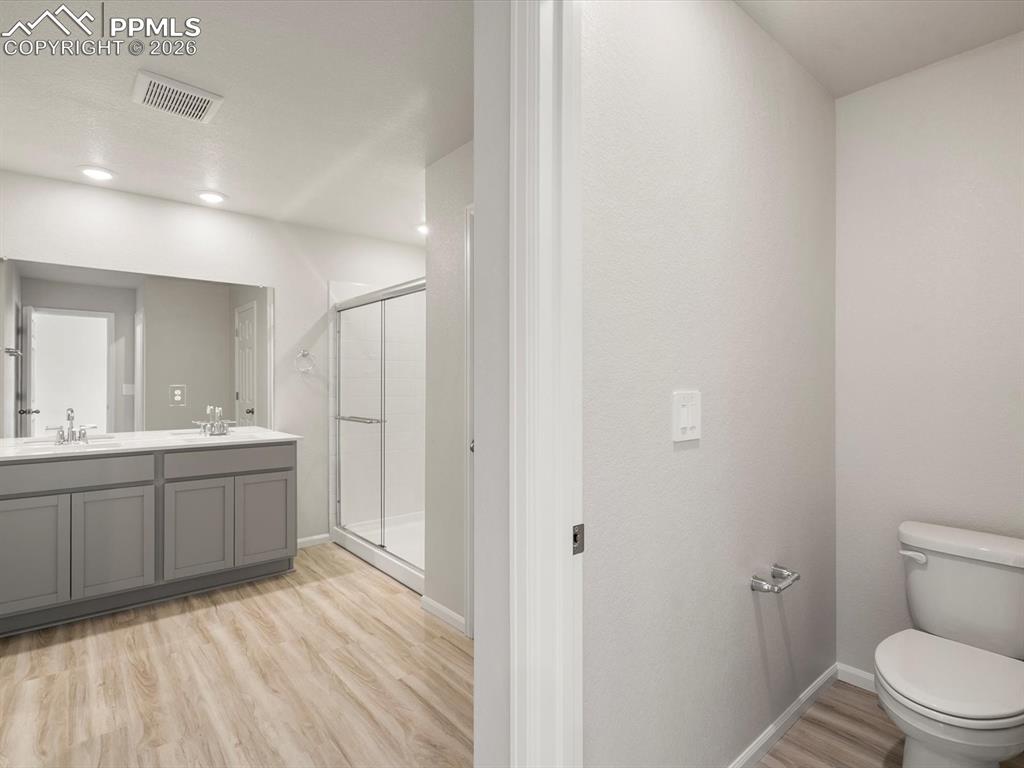 Bathroom with light wood-style flooring, a shower stall, and double vanity
