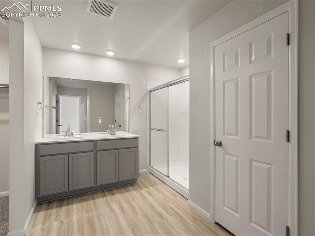 Full bath featuring a shower stall, double vanity, light wood-type flooring, and recessed lighting
