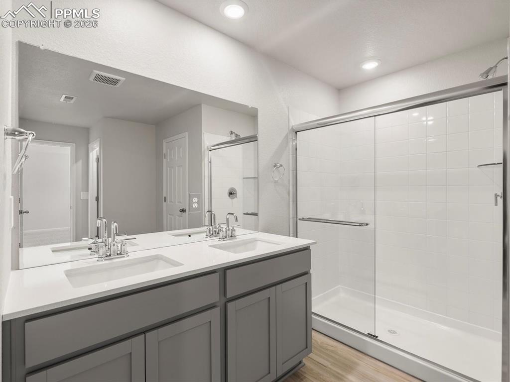 Full bathroom with a stall shower, double vanity, and light wood-type flooring