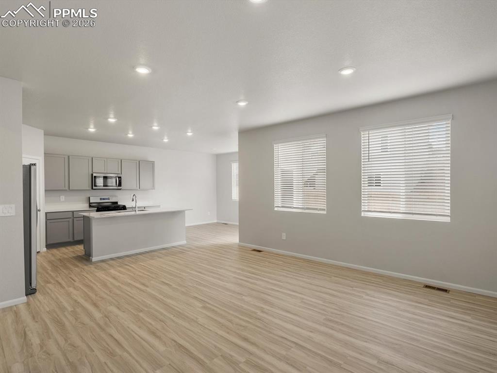 Kitchen featuring gray cabinetry, light wood-type flooring, open floor plan, an island with sink, and recessed lighting