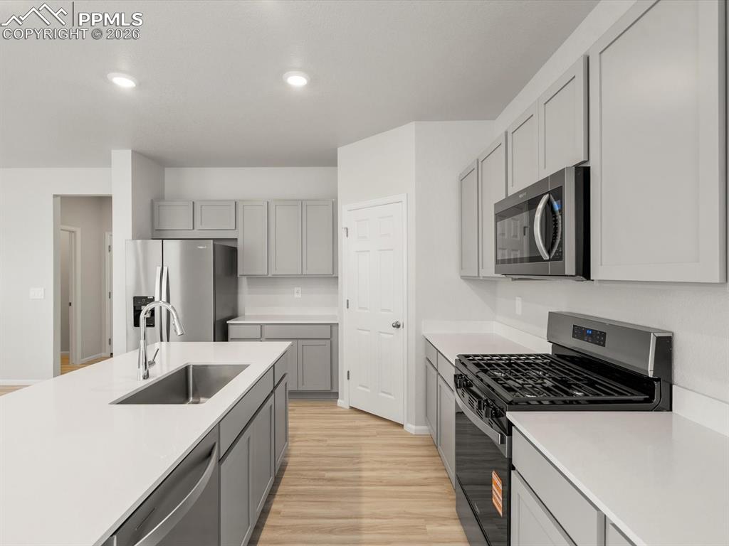 Kitchen featuring appliances with stainless steel finishes, light wood-style floors, gray cabinetry, recessed lighting, and light stone countertops