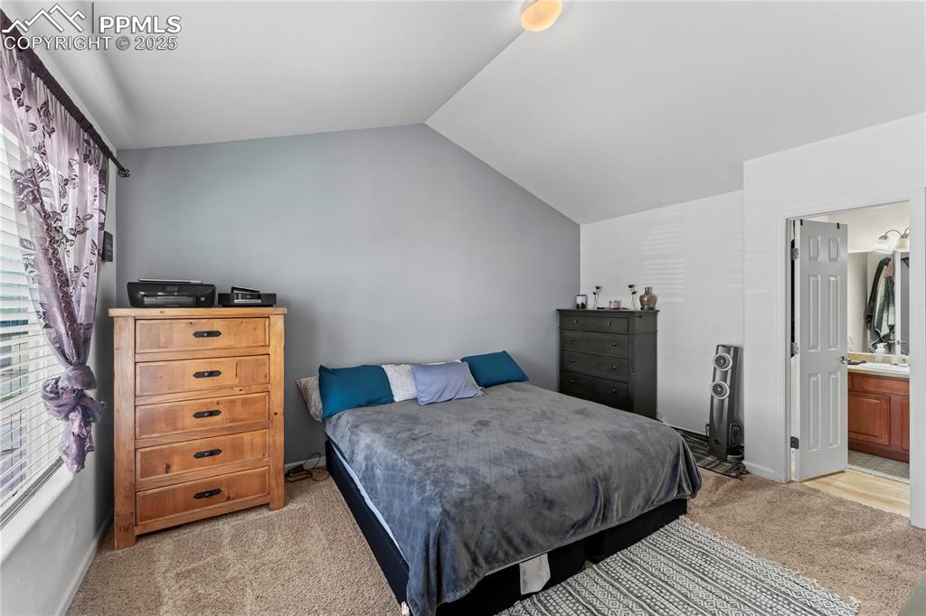 Bedroom with light carpet, lofted ceiling, and ensuite bathroom