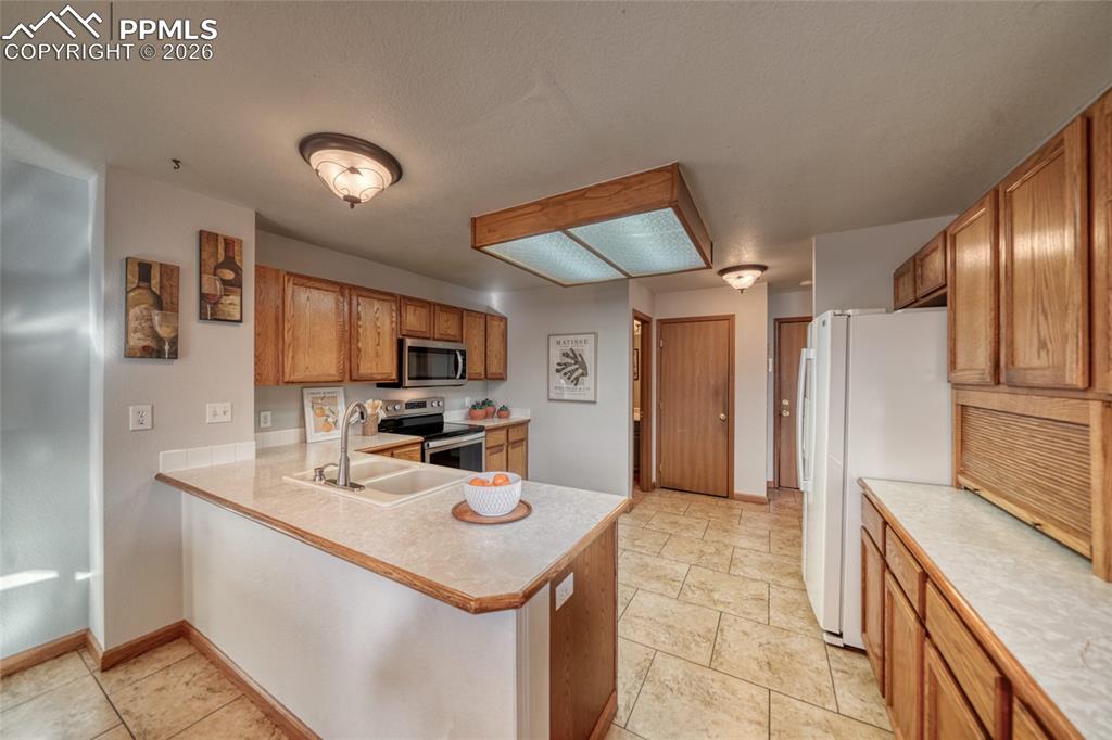 Kitchen featuring light countertops, stainless steel appliances, wood finish cabinetry, and a peninsula