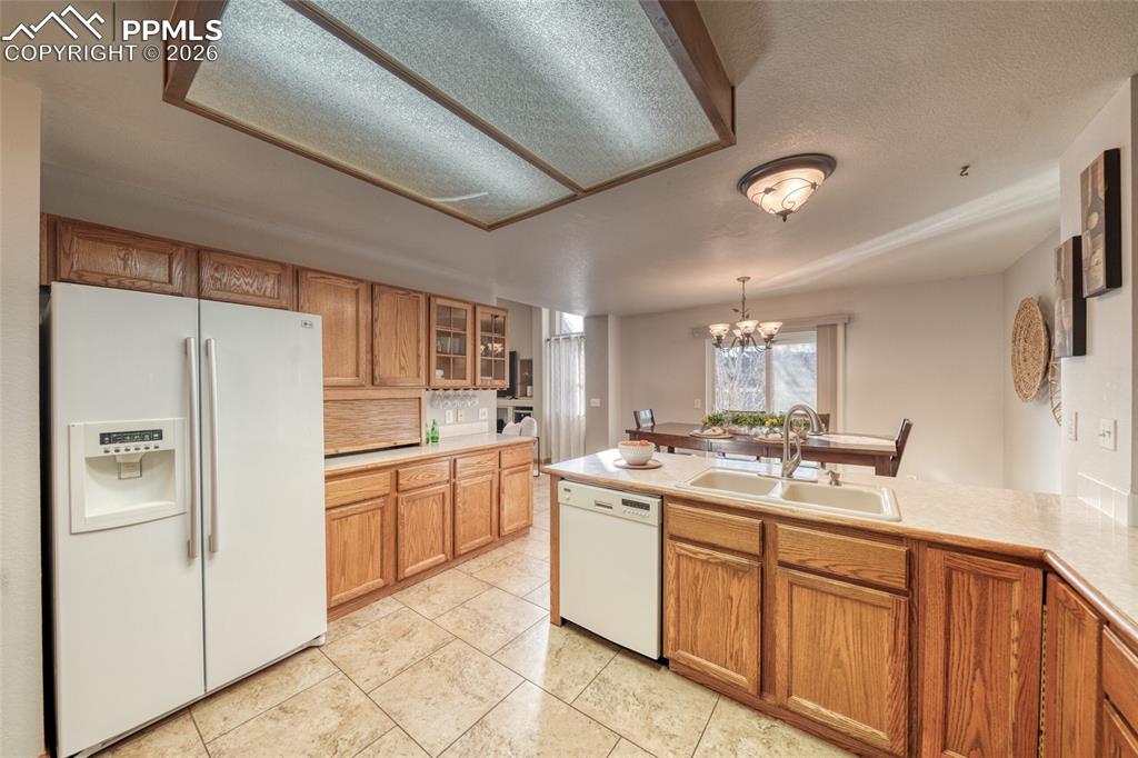Kitchen with white appliances, wood finish cabinetry, glass fronted cabinets, and suspended lighting