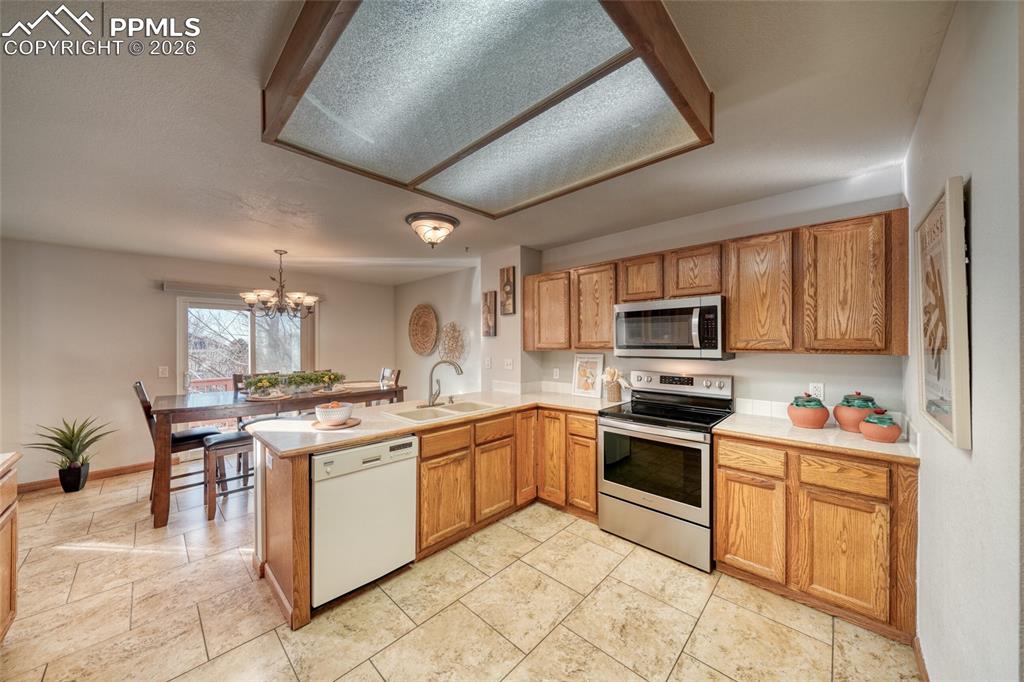Kitchen featuring stainless steel appliances, light countertops, a peninsula, a chandelier, and wood finish cabinetry