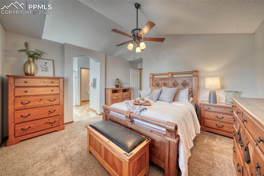 Bedroom featuring ensuite bath, arched walkways, light colored carpet, and ceiling fan