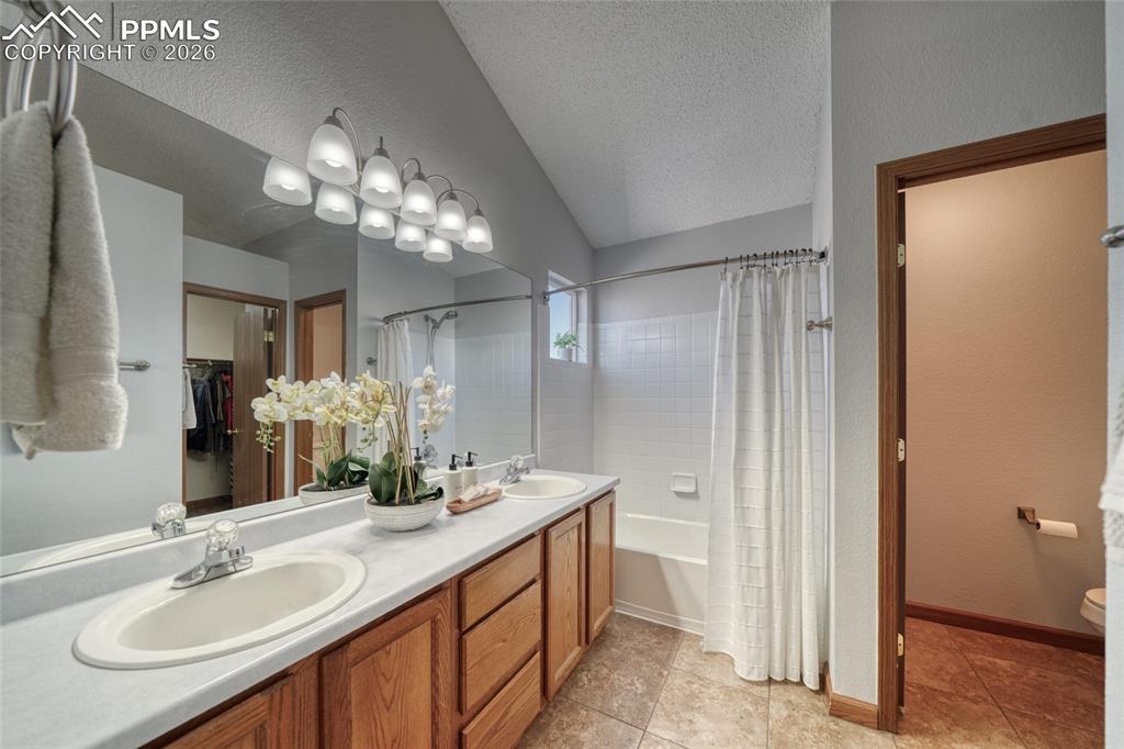 Bathroom featuring double vanity, a walk in closet, shower / bath combo, a textured wall, and light tile patterned floors