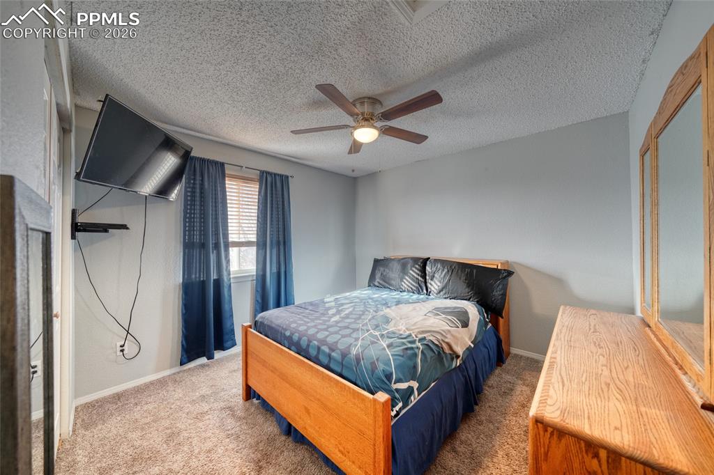 Bedroom with carpet floors, ceiling fan, and a textured ceiling