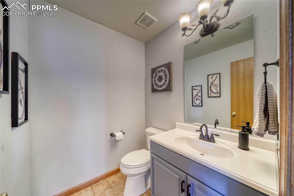 Half bathroom featuring vanity, a textured wall, a textured ceiling, and light tile patterned floors